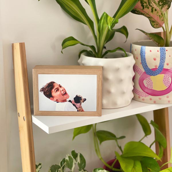 Mini landscape stone print of a smiling boy holding a dog – displayed on a shelf in a natural oak frame